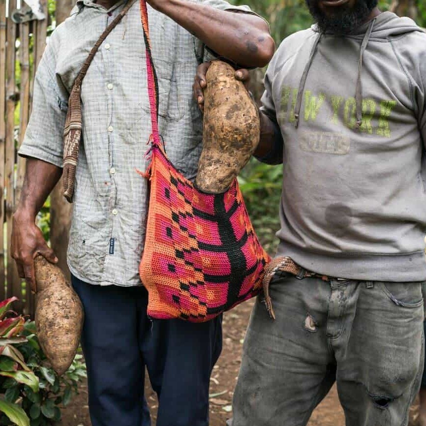 Relatives of Wasi and Lina Waukawe hold a bilum bag full of kaukau